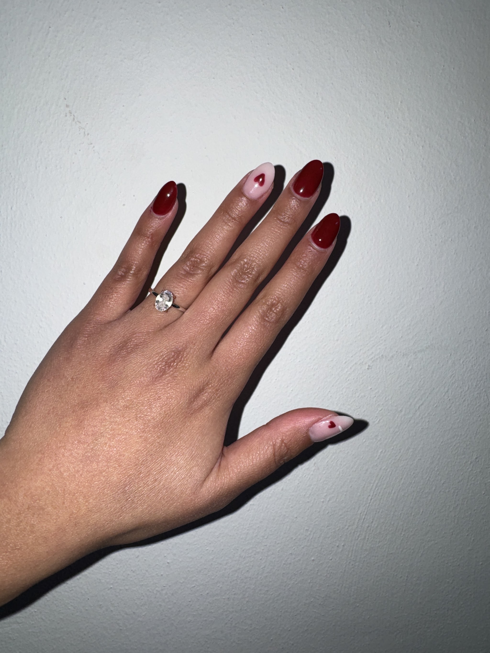 Hand met rode en lichtroze nagels, op twee nagels een rood hartje