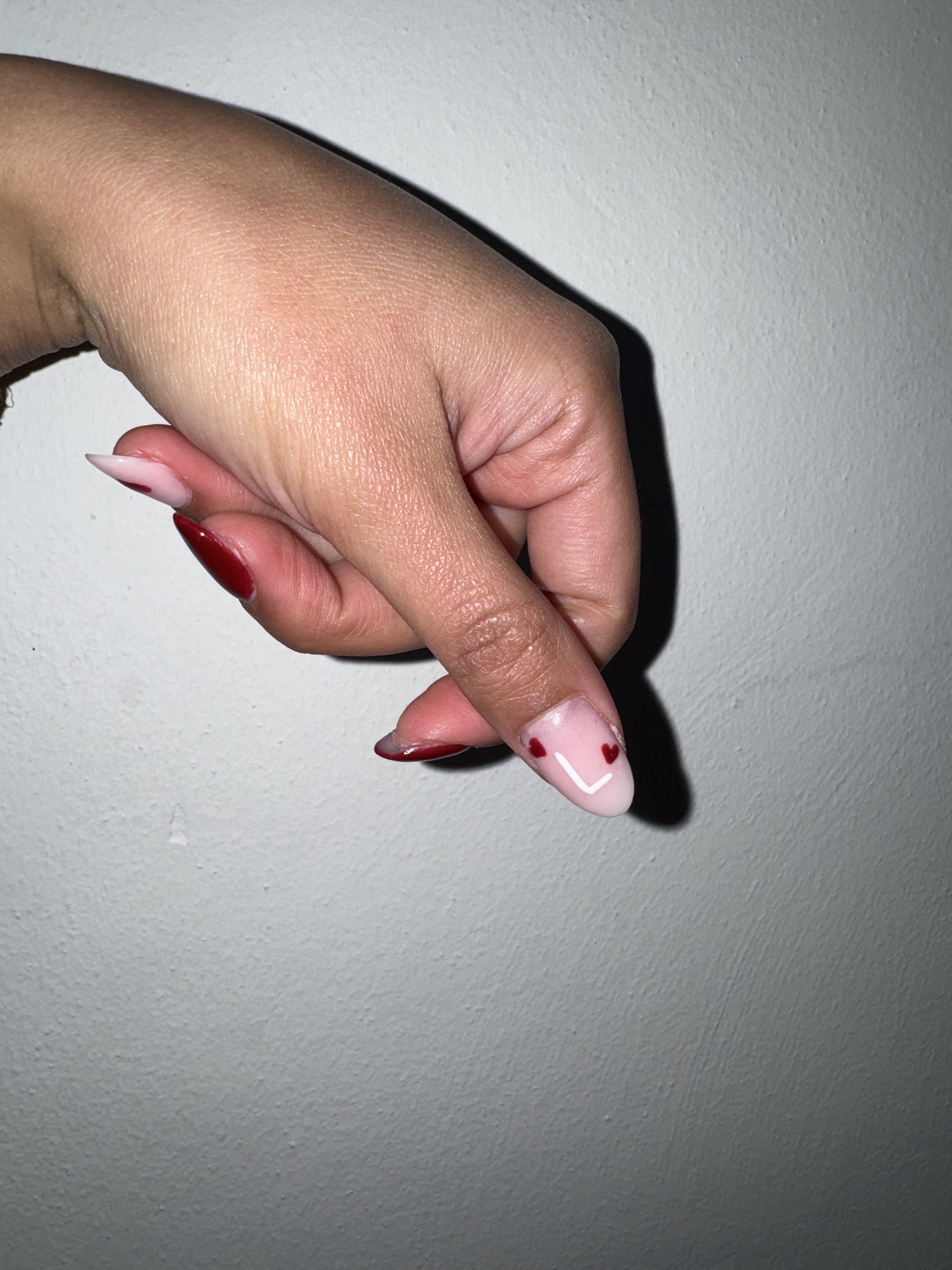 Lichtroze nagel met rode hartjes, naast rode nagels