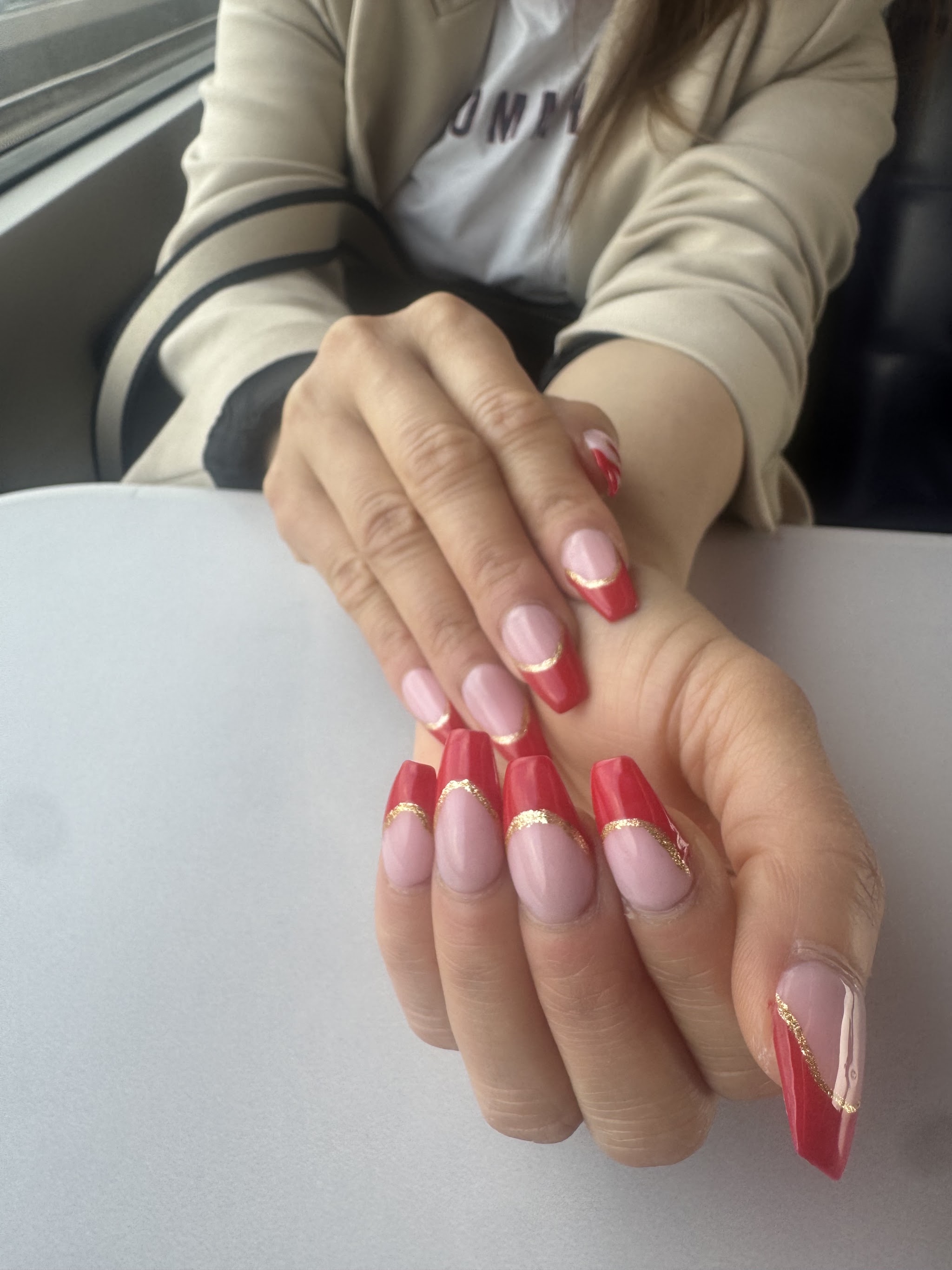 Handen met roze nagels en rode French tips met een gouden lijntje