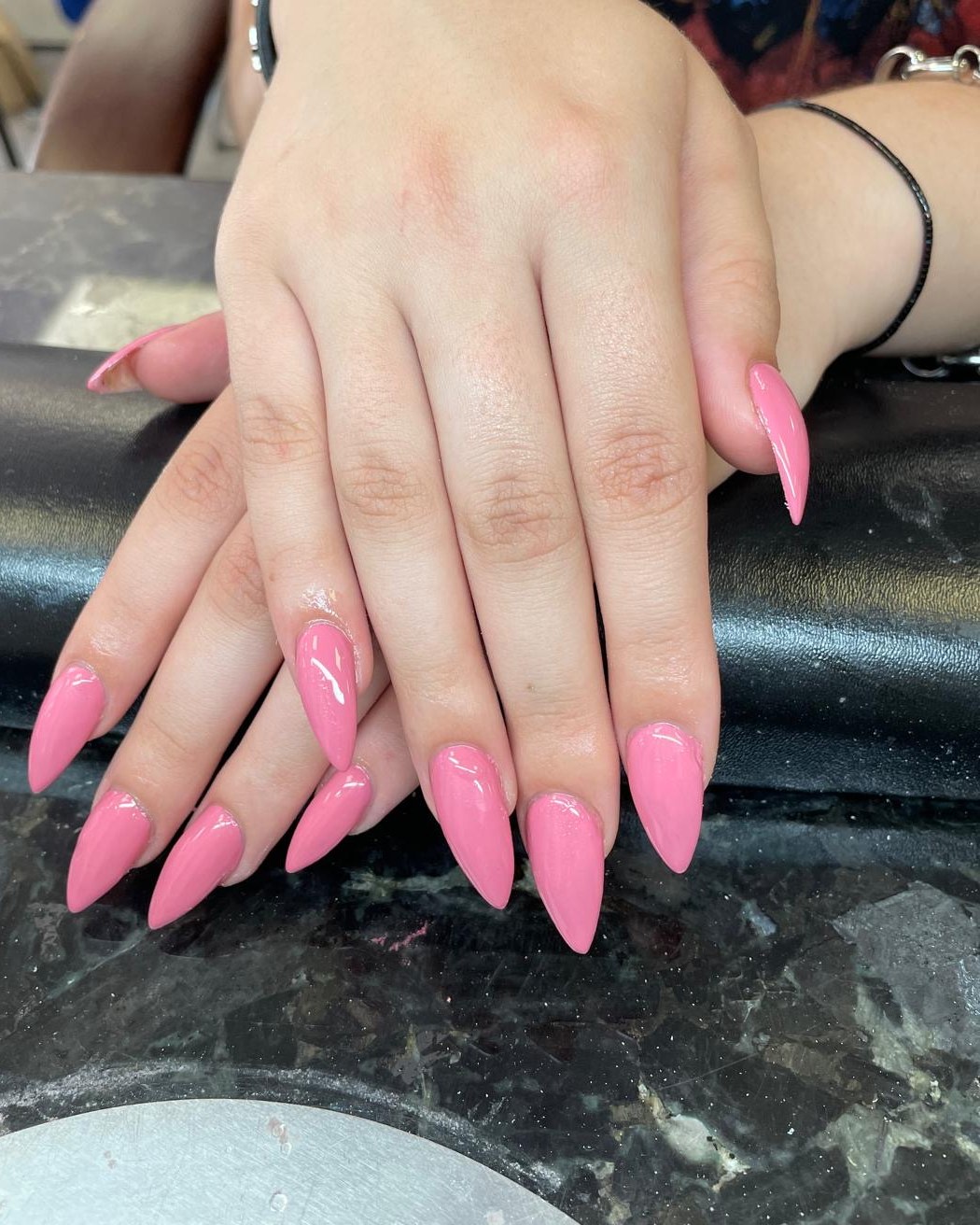 Roze acrylnagels in amandelvorm op de zwarte tafel van de salon